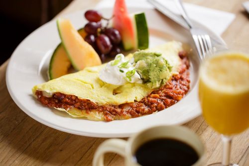 A plate with a cheese omelet topped with salsa, accompanied by fruit and a drink.
