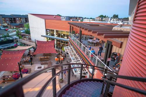 Aerial view of a modern outdoor dining area with seating, string lights, and nearby buildings at dusk.