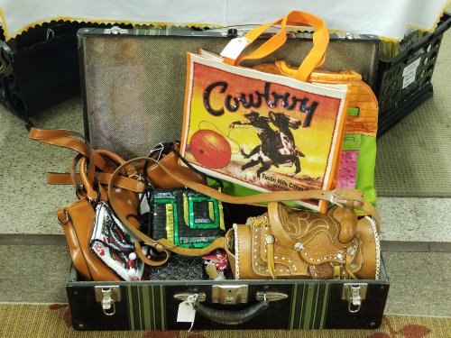 A vintage suitcase filled with colorful bags, including a cowboy-themed book and a decorative saddle.