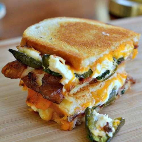 A stacked grilled cheese sandwich with melted cheese, jalapeños, and crispy layers on toasted bread.