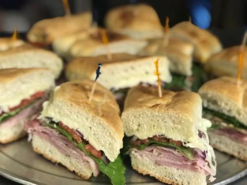 A platter of freshly made sandwiches with layers of ham, lettuce, tomato, and mayonnaise, secured with toothpicks.