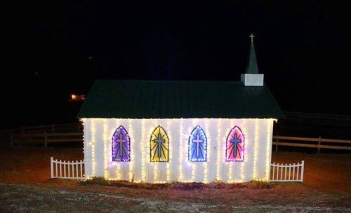 A small church decorated with colorful lights and illuminated stained glass windows at night.