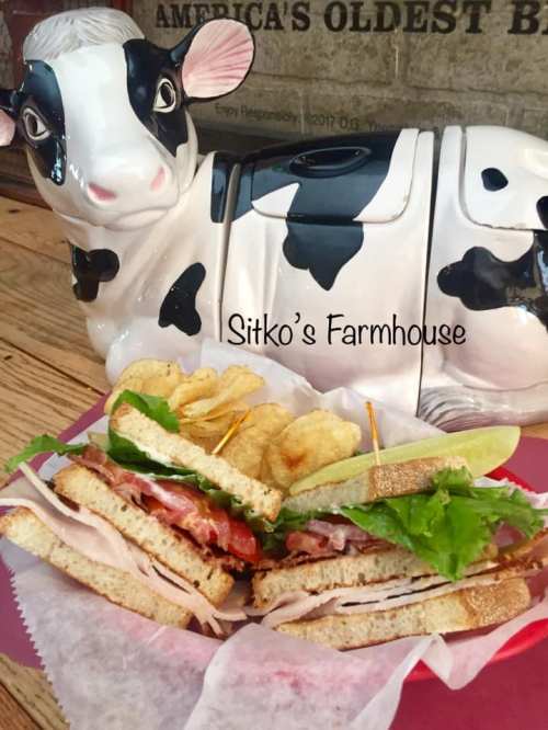 A sandwich with turkey, bacon, lettuce, and chips, next to a decorative cow-shaped container.