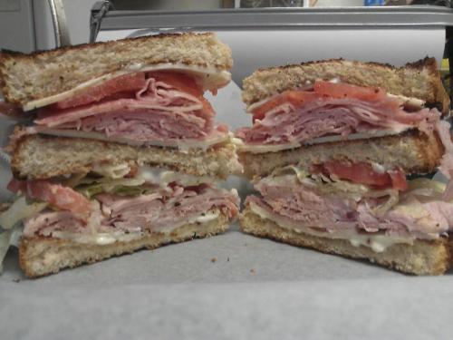 A stacked sandwich with layers of ham, turkey, lettuce, tomato, and mayonnaise between slices of whole grain bread.