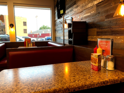 Cozy diner interior with red booths, a wooden wall, and a table set with condiments and a menu.