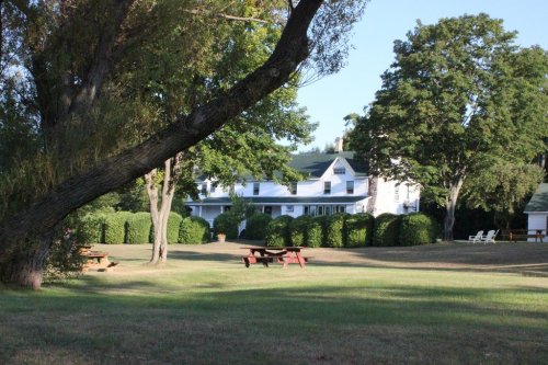 A spacious lawn with picnic tables, surrounded by trees and a large white house in the background.