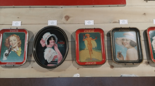 Vintage Coca-Cola trays featuring women in various poses and styles, displayed on a wooden wall.