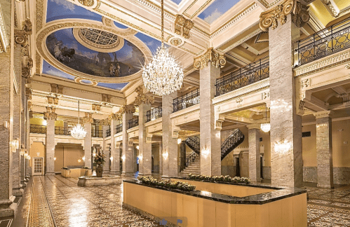 Elegant hotel lobby featuring marble columns, a grand chandelier, and a beautifully painted ceiling.