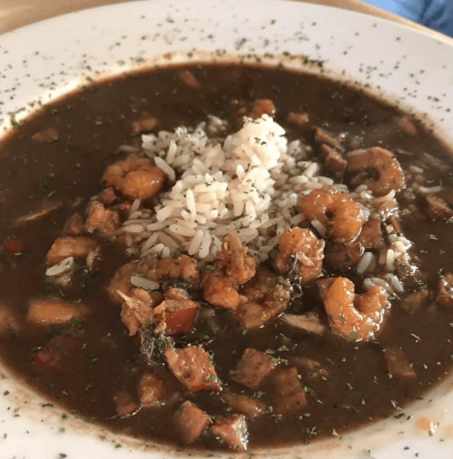 A bowl of gumbo with shrimp, sausage, and rice, garnished with parsley.