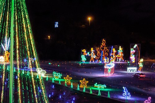 Colorful holiday lights illuminate a festive scene with various shapes and decorations, including a large Christmas tree.