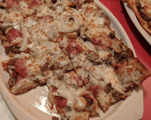 A close-up of a pizza topped with cheese, pepperoni, sausage, onions, and mushrooms on a white plate.