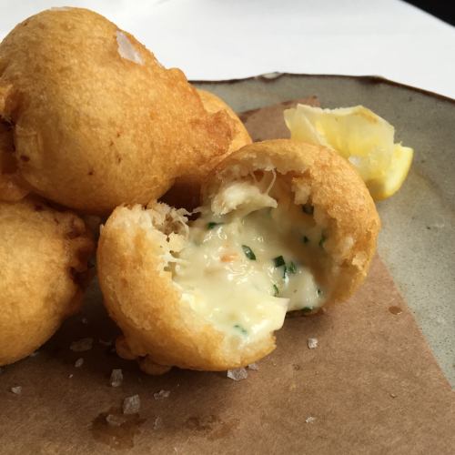 Golden, crispy fritters on a plate, one cut open to reveal creamy filling with herbs, served with a lemon wedge.
