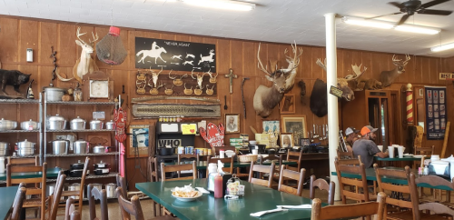 A rustic diner with wooden walls, mounted animal heads, and a few patrons sitting at green tables.