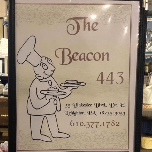 A sign for "The Beacon" restaurant featuring a cartoon chef holding plates, with address and contact information.