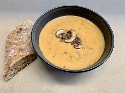 A bowl of creamy mushroom soup with sliced mushrooms, accompanied by a piece of rustic bread on the side.