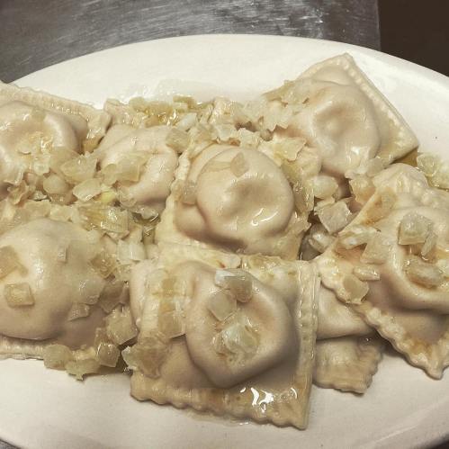 A plate of ravioli topped with chopped onions and a light sauce, arranged neatly.