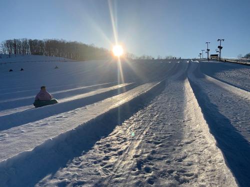 A snowy hill with multiple tubing lanes, a person sitting on a tube, and the sun setting in the background.