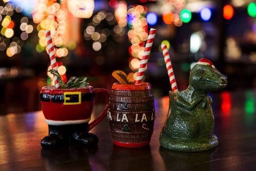 Three festive holiday-themed cocktails with colorful straws, set against a backdrop of twinkling lights.