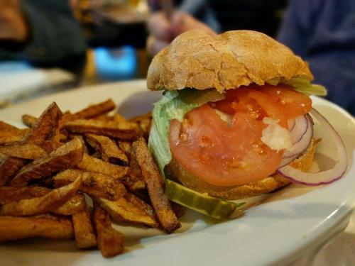 A sandwich with lettuce, tomato, and onion, served with a side of crispy French fries on a white plate.