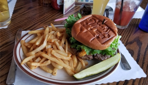 A burger with lettuce on a plate, accompanied by a side of French fries and a pickle.