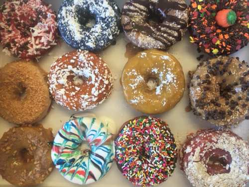A box of assorted donuts featuring various toppings and colors, including sprinkles, chocolate, and coconut.
