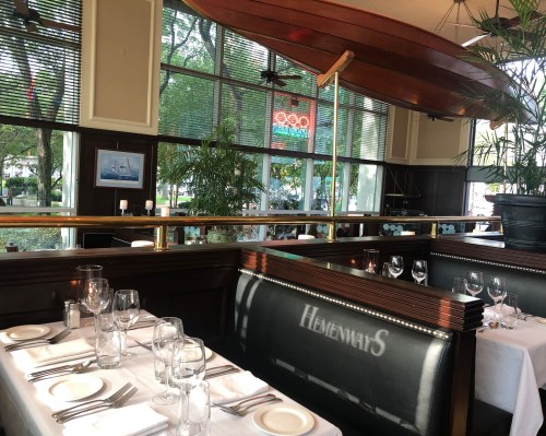 A cozy restaurant interior with wooden accents, tables set for dining, and a vintage boat hanging above.