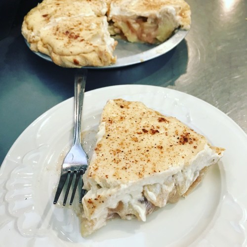 A slice of creamy pie topped with cinnamon on a white plate, with a whole pie in the background.