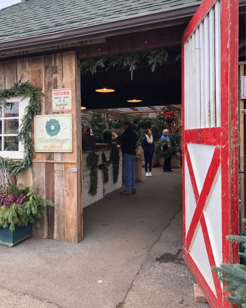 A rustic garden shop entrance decorated with greenery, featuring customers browsing inside.