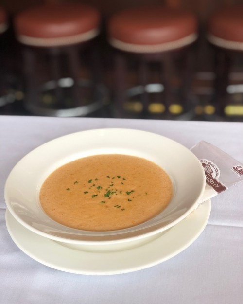 A bowl of creamy soup garnished with herbs, placed on a white tablecloth with a napkin beside it.
