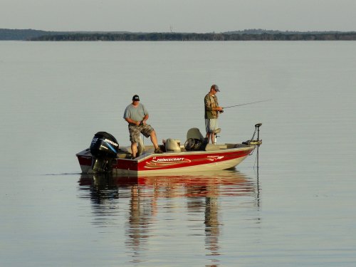 Two men fishing from a small boat on a calm lake, with a clear sky and reflections on the water.