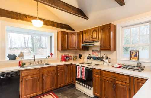 Cozy kitchen with wooden cabinets, a window, and appliances, featuring a red and white color scheme and rustic beams.