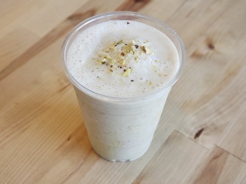 A frothy beverage in a clear cup, topped with crushed nuts, sitting on a wooden surface.