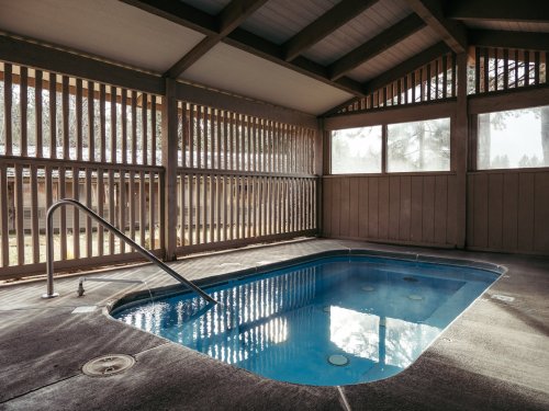 Indoor pool with a blue water, surrounded by wooden slats and large windows, creating a serene atmosphere.