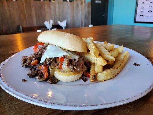 A sandwich filled with beef, peppers, and onions, served with crinkle-cut fries on a white plate.