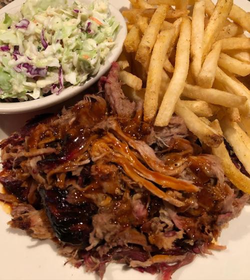 A plate featuring pulled pork with barbecue sauce, coleslaw, and crispy French fries.