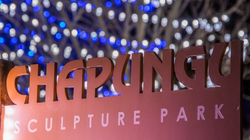Sign for Chapungu Sculpture Park illuminated against a backdrop of blue and white bokeh lights.