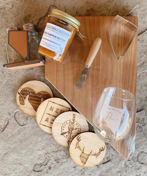 A wooden cutting board with a jar of pumpkin butter, a knife, coasters, and a wine glass on a textured surface.