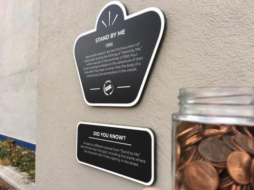 Sign about the film "Stand By Me" with a jar of coins in the foreground, set against a wall.