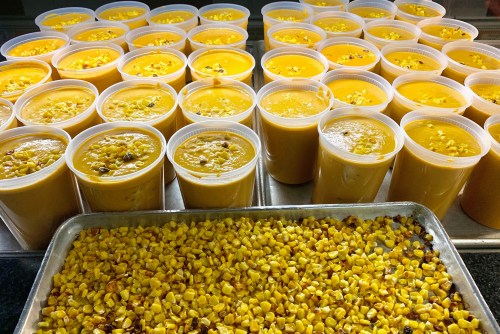A tray of roasted corn sits in front of numerous cups filled with a yellow, creamy dessert.