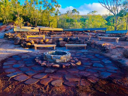 A circular stone fire pit surrounded by benches in a natural outdoor setting with trees and blue sky.