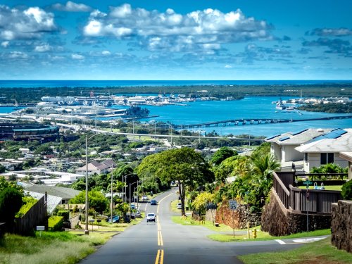 Scenic view of a coastal town with a winding road, lush greenery, and a harbor under a bright blue sky.