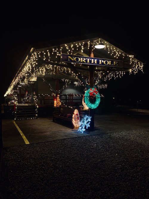 A festive North Pole sign adorned with colorful lights and holiday decorations at night.