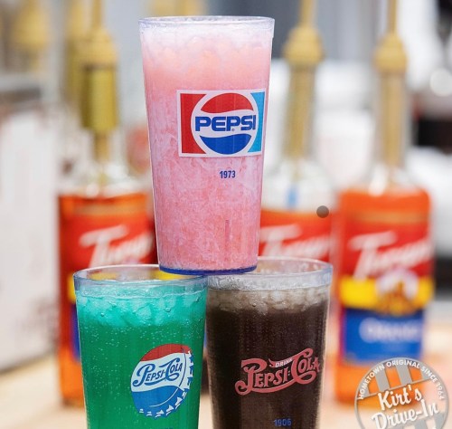 Three colorful drinks in branded cups: pink, green, and dark brown, with soda dispensers in the background.