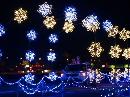 A car drives under a colorful arch of snowflake lights at night, creating a festive atmosphere.