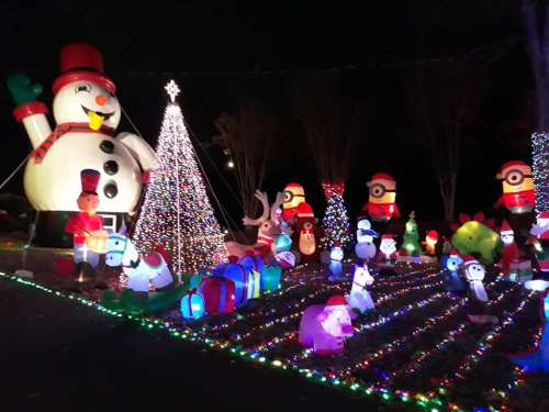 A festive display featuring inflatable characters, a snowman, Christmas tree, and colorful lights in a nighttime setting.