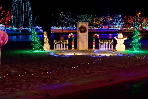 A festive winter scene with colorful lights, a snowman, a snowwoman, and a decorated door surrounded by candy canes.