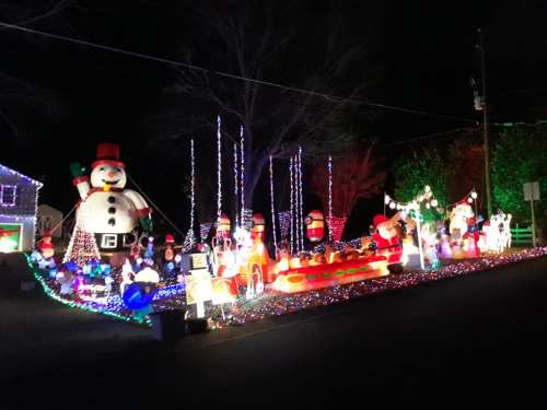 A festive display of colorful Christmas lights and inflatable decorations, including snowmen and Santa, at night.