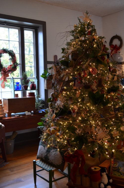 A decorated Christmas tree with lights and ornaments, beside a window with wreaths and a cozy interior setting.