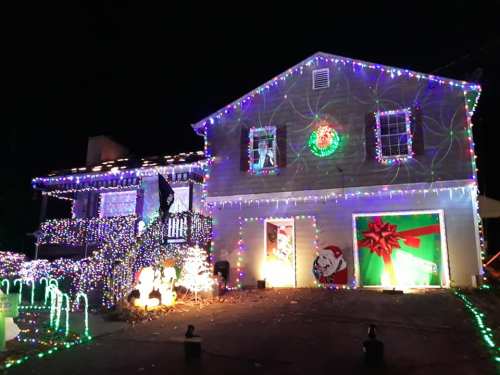 A house decorated with colorful Christmas lights, featuring a large gift and festive decorations in the yard.