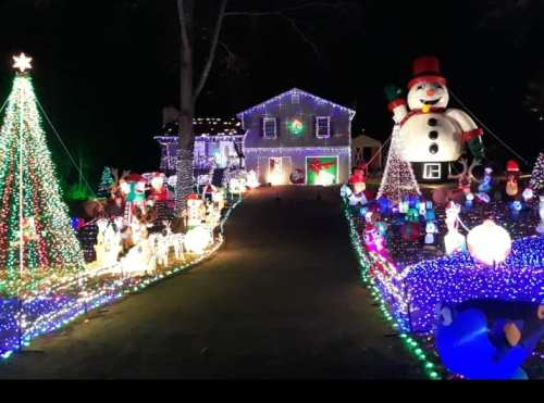 A festive house decorated with colorful lights, inflatable snowman, and holiday decorations lining the driveway.